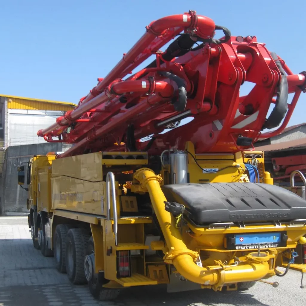 Rote Betonpumpe mit ausgefahrenem Verteilermast auf gelbem LKW-Chassis