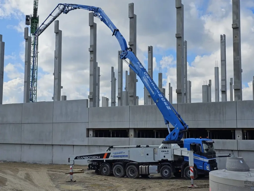 Blaue Autobetonpumpe mit ausgefahrenem Mast vor Stahlbeton-Rohbau